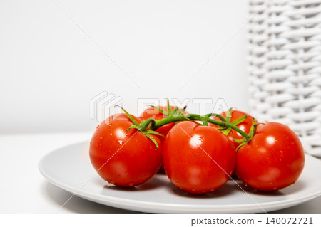A bunch of ripe red tomatoes on a green vine placed on a white plate. Minimalist background with copy space for text. Isolated healthy eating. A bunch of ripe red tomatoes on a green vine placed on a white plate. Minimalist background with copy space for text. Isolated healthy eating. 140072721