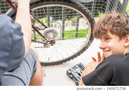 A man teaches his teenage son how to fix a vintage red bicycle on a cozy balcony, showing family support, teamwork, and learning valuable skills. A man teaches his teenage son how to fix a vintage red bicycle on a cozy balcony, showing family support, teamwork, and learning valuable skills. 140072736