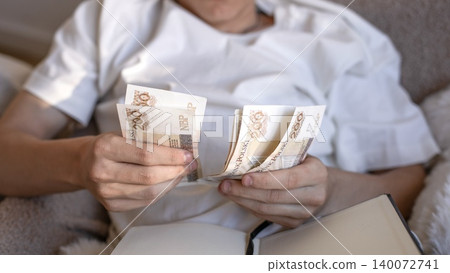 A close up of a man counting 200 polish zloty banknotes while calculating business expenses, loan payments or domestic taxes in a notebook. A close up of a man counting 200 polish zloty banknotes while calculating business expenses, loan payments or domestic taxes in a notebook. 140072741