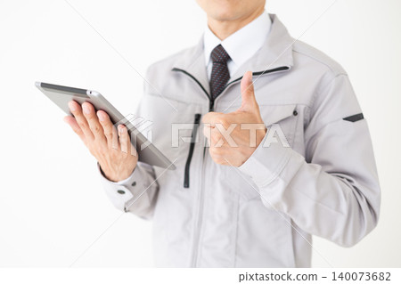 身穿灰色工作服的中年商務人士，手持平板電腦，豎起大拇指，背景為白色。 140073682