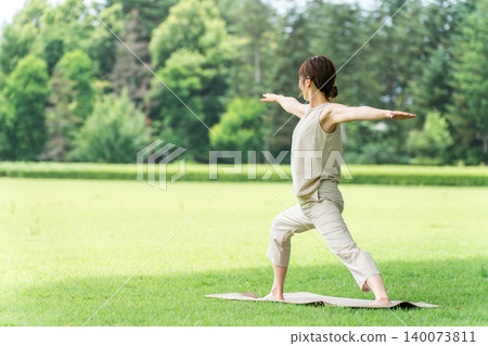 A young Asian woman doing park yoga, yoga, Pilates, and stretching in a park (Warrior Pose). A young Asian woman doing park yoga, yoga, Pilates, and stretching in a park (Warrior Pose). 140073811