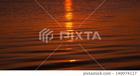 The shimmering surface of the lake bathed in the morning sun, with the reflections of the water in the background. The shimmering surface of the lake bathed in the morning sun, with the reflections of the water in the background. 140074117
