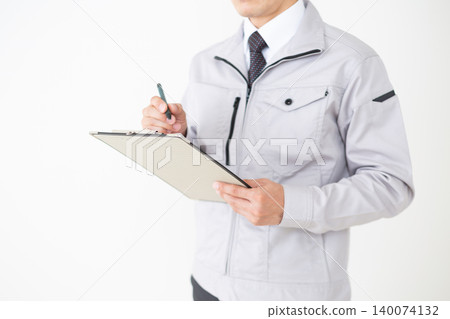 一位身穿灰色工作服的中年商人,在白色背景下查看活頁夾中的文件。 一位身穿灰色工作服的中年商人,在白色背景下查看活頁夾中的文件。 140074132