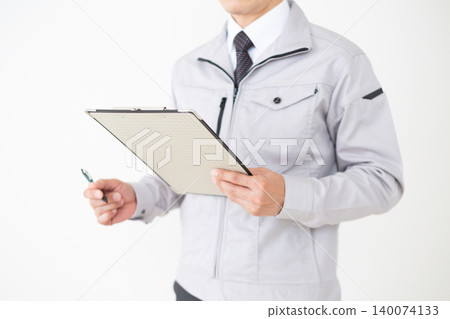 一位身穿灰色工作服的中年商人,在白色背景下查看活頁夾中的文件。 一位身穿灰色工作服的中年商人,在白色背景下查看活頁夾中的文件。 140074133