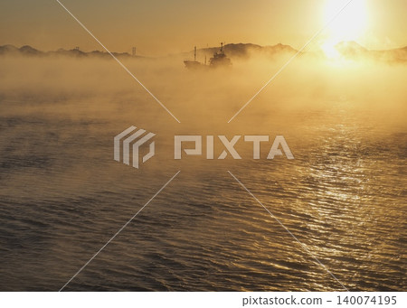一艘船航行在晨曦照耀下的海霧中。 一艘船航行在晨曦照耀下的海霧中。 140074195
