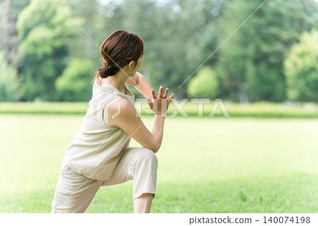 A young Asian woman doing yoga, Pilates, and stretching (player's twist) in a park. A young Asian woman doing yoga, Pilates, and stretching (player's twist) in a park. 140074198