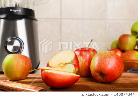 Fresh red apples, whole and sliced, on a wooden cutting board with a kitchen knife, next to a stainless steel blender. A healthy food preparation scene. High quality photo Fresh red apples, whole and sliced, on a wooden cutting board with a kitchen knife, next to a stainless steel blender. A healthy food preparation scene. High quality photo 140074344