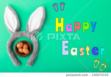 Festive Happy Easter greeting featuring fluffy bunny ears encircling a nest of speckled eggs, colorful text, and bunny tracks on a bright green background. Top view, flat lay. High quality photo Festive Happy Easter greeting featuring fluffy bunny ears encircling a nest of speckled eggs, colorful text, and bunny tracks on a bright green background. Top view, flat lay. High quality photo 140074350