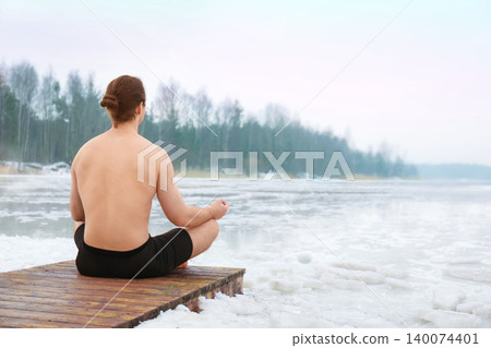 Shirtless man with long hair in a bun sitting in a lotus meditation pose on a wooden pier by a frozen, icy lake during winter. High quality photo Shirtless man with long hair in a bun sitting in a lotus meditation pose on a wooden pier by a frozen, icy lake during winter. High quality photo 140074401