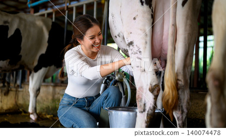 Female farmer manually milking dairy cow into bucket in traditional farm setting Female farmer manually milking dairy cow into bucket in traditional farm setting 140074478