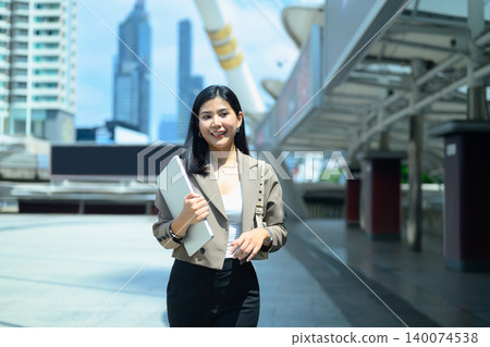 Businesswoman with holding laptop looking camera in urban cityscape Businesswoman with holding laptop looking camera in urban cityscape 140074538