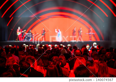 Crowd watching live music concert performance on illuminated red stage with band and singer Crowd watching live music concert performance on illuminated red stage with band and singer 140074567