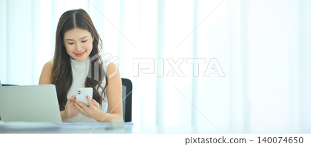 Businesswoman checking smartphone at desk in bright office 140074650