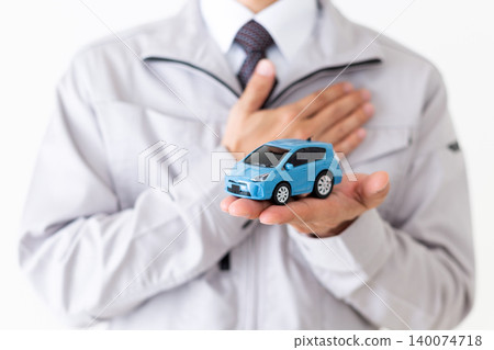 A middle-aged businessman in gray work clothes holding a model car against a white background. A middle-aged businessman in gray work clothes holding a model car against a white background. 140074718