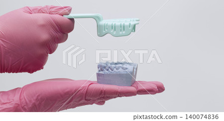 Dentist hands in pink gloves holding a purple plaster cast of teeth and lifting an empty impression tray. Copy space. Dentist hands in pink gloves holding a purple plaster cast of teeth and lifting an empty impression tray. Copy space. 140074836