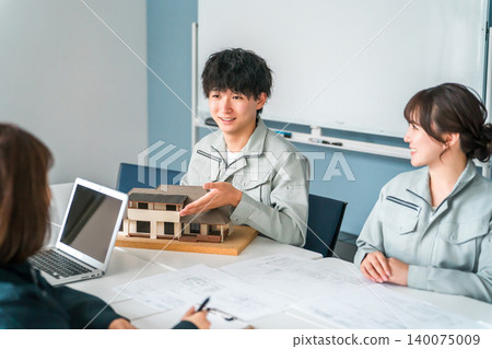 Male and female businessmen in the construction and building industry wearing work clothes negotiating, explaining and presenting using a house model Male and female businessmen in the construction and building industry wearing work clothes negotiating, explaining and presenting using a house model 140075009