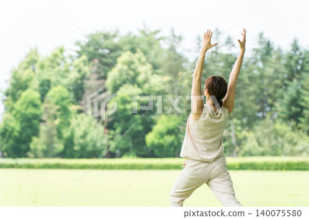 A woman's back view while doing yoga, stretching, and flexibility exercises in a park (high lunge pose). 140075580