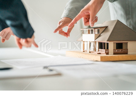 A businessman's hands pointing to a model house and blueprints. A businessman's hands pointing to a model house and blueprints. 140076229