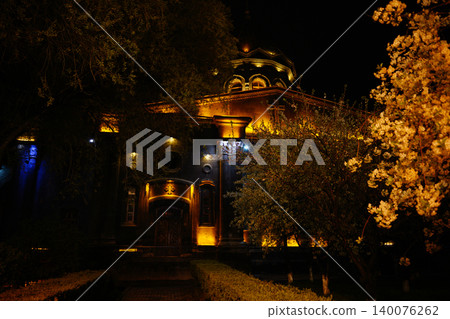 Illuminated historic church structure at night surrounded by flowering trees Illuminated historic church structure at night surrounded by flowering trees 140076262