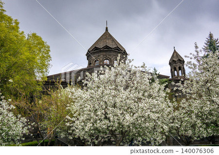 White flowering cherry trees frame old stone church under gray sky 140076306
