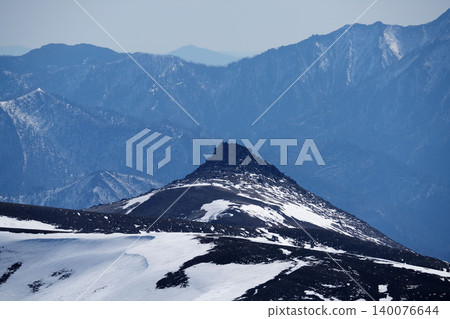 The black, dome-shaped rock formations of Mount Asahidake in Hokkaido, with the blue mountain range in the distance. 140076644