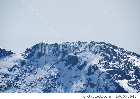 A close-up of the sharp, rocky ridges of the snow-covered mountains of Asahidake, Hokkaido, against a blue sky. A close-up of the sharp, rocky ridges of the snow-covered mountains of Asahidake, Hokkaido, against a blue sky. 140076645