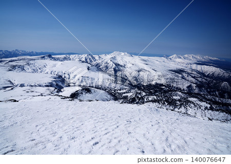 A panoramic view of snow-covered mountains from the snowfield at the summit of Mt. Asahidake in Hokkaido, under a blue sky. A panoramic view of snow-covered mountains from the snowfield at the summit of Mt. Asahidake in Hokkaido, under a blue sky. 140076647