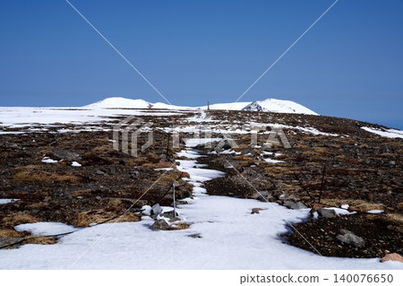 The snow-covered rocky terrain and summit of Mt. Asahidake in Hokkaido, under a clear blue sky. 140076650