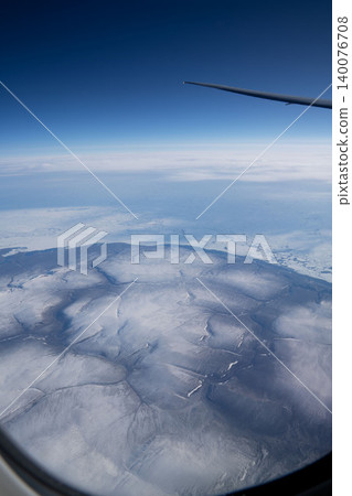 A high-altitude aerial photograph showing the snowfields of the Arctic Circle and the wing of an airplane as seen from the window over Hokkaido. 140076708