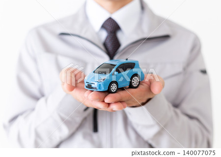 A middle-aged businessman in gray work clothes holding a model car against a white background. A middle-aged businessman in gray work clothes holding a model car against a white background. 140077075