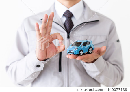 身穿灰色工作服的中年商人,手持汽車模型,在白色背景前擺出圓形姿勢。 身穿灰色工作服的中年商人,手持汽車模型,在白色背景前擺出圓形姿勢。 140077188