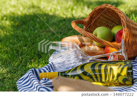 Picnic basket with wine, fruits, and baguette on a sunny green meadow 140077222