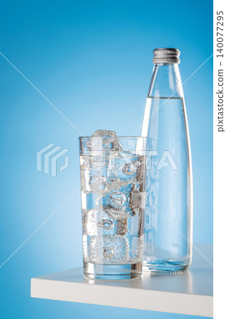 Glass of sparkling water with ice cubes on blue background minimal Glass of sparkling water with ice cubes on blue background minimal 140077295