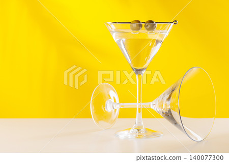 Classic martini cocktail with olives in glass on yellow background Classic martini cocktail with olives in glass on yellow background 140077300