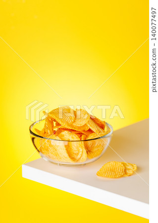 Bowl of potato chips on yellow background minimal snack composition Bowl of potato chips on yellow background minimal snack composition 140077497