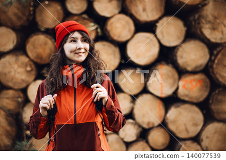 Smiling woman stands in front of stacked timber logs in woodland area. Woman forest inspector, female industrial professional, environmental auditor at work. Smiling woman stands in front of stacked timber logs in woodland area. Woman forest inspector, female industrial professional, environmental auditor at work. 140077539