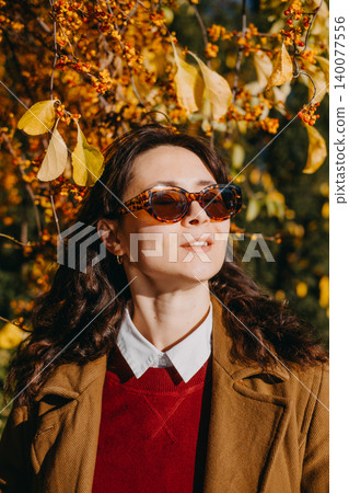 Woman poses outdoors with autumn branches while wearing sunglasses. Autumn sun protection awareness, uv safety lifestyle campaign, transitional seasonal skin health. Woman poses outdoors with autumn branches while wearing sunglasses. Autumn sun protection awareness, uv safety lifestyle campaign, transitional seasonal skin health. 140077556