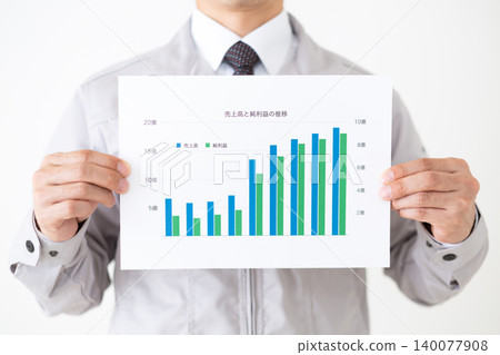 身穿灰色工作服的中年商人，在白色背景前手持業績圖表。 140077908