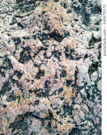 Close look at a sea rock surface with weathered texture. The rock shows volcanic patterns in pink, white, and black colors. This formation gives insight into natural processes over time. Close look at a sea rock surface with weathered texture. The rock shows volcanic patterns in pink, white, and black colors. This formation gives insight into natural processes over time. 140078372
