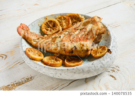 Red snapper served with roasted lemon slices on a white plate on a wooden table Red snapper served with roasted lemon slices on a white plate on a wooden table 140078535