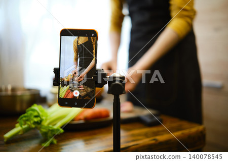 Cooking demonstration with smartphone capturing food preparation in a kitchen setting 140078545