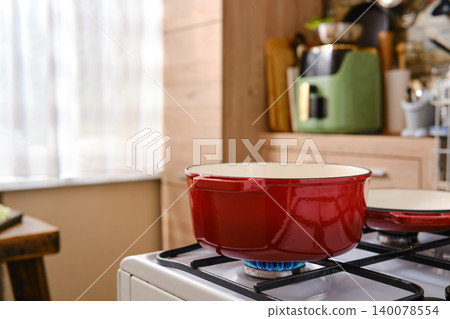 Cooking in a red pot on a gas stove in a kitchen with wood and light colors Cooking in a red pot on a gas stove in a kitchen with wood and light colors 140078554