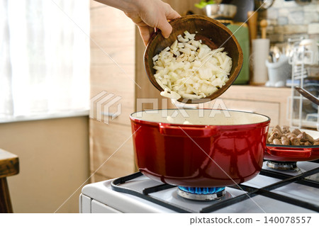 Cooking onions in a red pot on the stove in a kitchen setting during the day Cooking onions in a red pot on the stove in a kitchen setting during the day 140078557