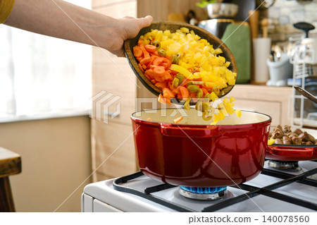 Chopping and adding colorful vegetables to a red pot on the stove in a kitchen Chopping and adding colorful vegetables to a red pot on the stove in a kitchen 140078560
