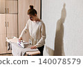 Woman ironing clothes in a room with patterned wall 140078579