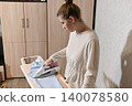 Woman ironing clothes in a room with patterned wall 140078580