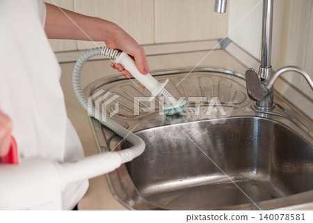 Cleaning a kitchen sink with a handheld steam cleaner during a home cleaning session 140078581