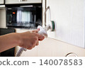 Cleaning the kitchen cabinets with a steamer near a microwave in afternoon light 140078583