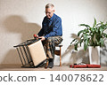 Man fixes wooden chair in a home setting with a plant nearby 140078622