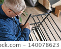 Man fixes wooden chair in a home setting with a plant nearby 140078623
